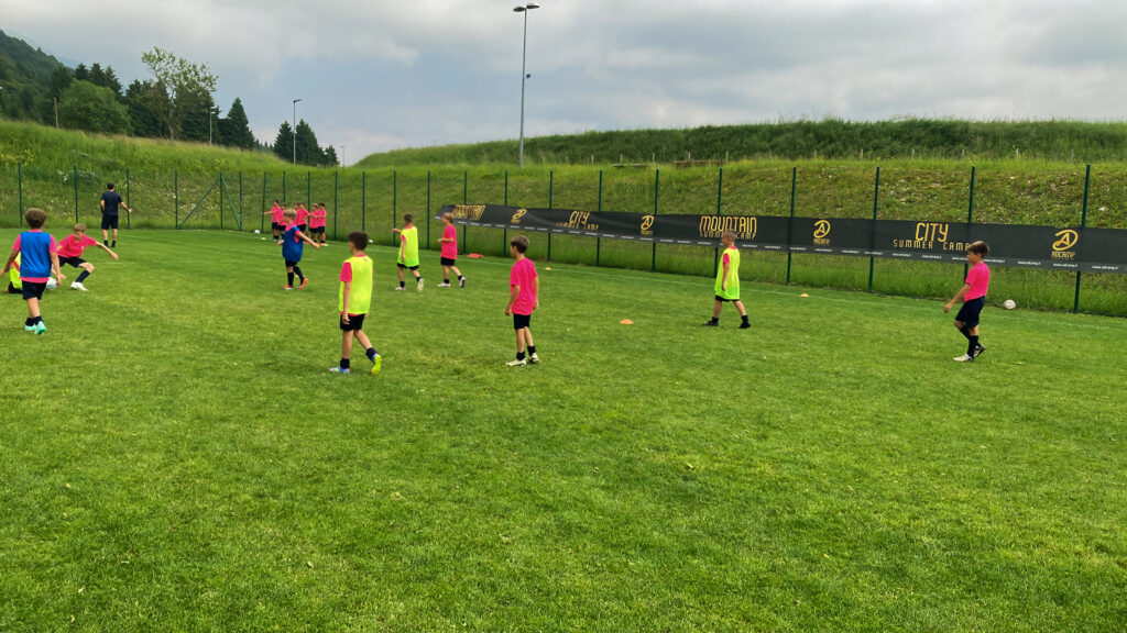 Gruppo di ragazzi suddivisi in due squadre, rispettivamente con maglie gialle e fucsia del kit ADCamp, che giocano a calcio.