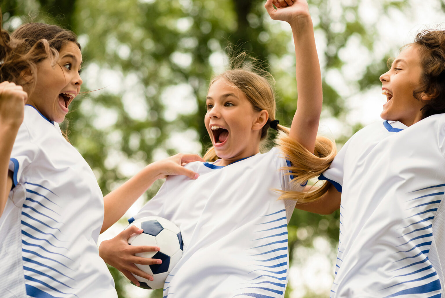 Tre ragazze che esultano mentre giocano a calcio.